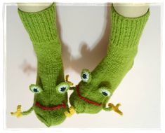 two green knitted frog socks with eyes and legs hanging off the side of a white wall