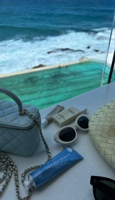 a purse, sunglasses, and other items are sitting on a table next to the ocean