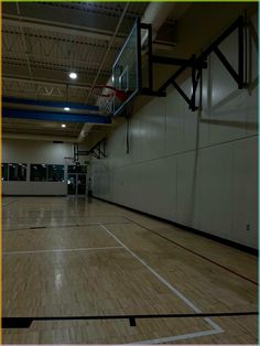 an indoor basketball court with hard wood flooring and lights on the side wall is empty