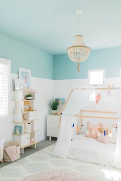 a white bed sitting in a bedroom under a chandelier next to a window