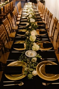 a long table is set with black and gold plates, silverware, and flowers