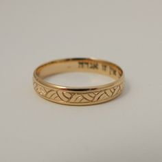 a gold wedding ring with an engraved design on the outside and inside, sitting on a white surface