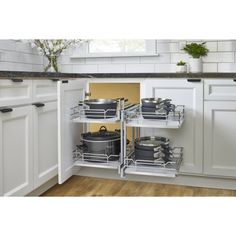 an open kitchen cabinet with pots and pans on the bottom shelf in front of white cabinets