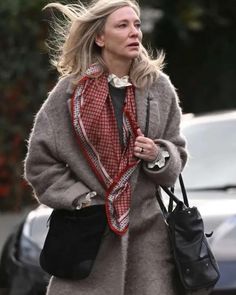 a woman walking down the street with a handbag in her other hand while wearing a coat and scarf