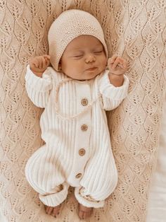 a baby is laying down wearing a white knitted outfit and a beanie hat