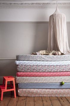 a stack of mattresses sitting on top of a wooden floor next to a red chair