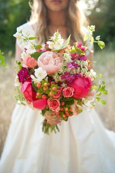 a woman holding a bouquet of flowers in her hands and wearing a white wedding dress