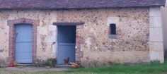 three chickens are standing in front of an old brick building with blue doors and windows