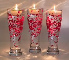 three tall vases with candles in them on a white tableclothed surface, decorated with red flowers and hearts