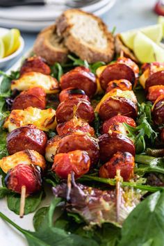 a platter filled with skewered meats and vegetables on top of greens