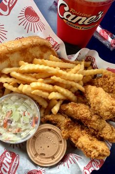 fried chicken, french fries and coleslaw on a paper wrapper next to a drink