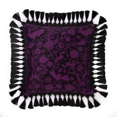 a purple and black pillow with tassels on the edges is sitting on a white surface