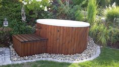 an outdoor hot tub in the middle of a garden with rocks and plants around it