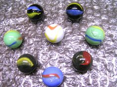 six marbles with different colors and shapes on a silver surface