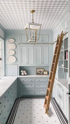 a ladder in the middle of a kitchen with white cabinets and blue walls, along with black and white checkered floor tiles