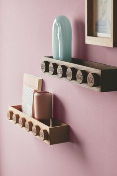 two wooden shelfs with magnets and cups on them against a pink painted wall