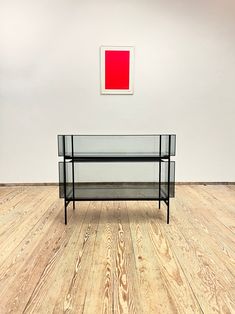 a glass table sitting on top of a hard wood floor next to a red painting