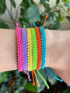 a woman's arm with multicolored bracelets on it and a potted plant in the background