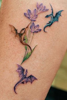 a woman's thigh with purple flowers and dragon tattoos on it