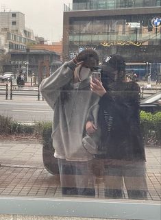 two people are standing in front of a window and talking on their cell phones while one person is taking a selfie