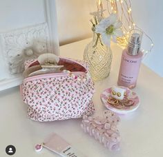 a pink purse sitting on top of a white table next to a bottle of perfume