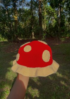 a red and white crocheted mushroom hat held up by someone's hand