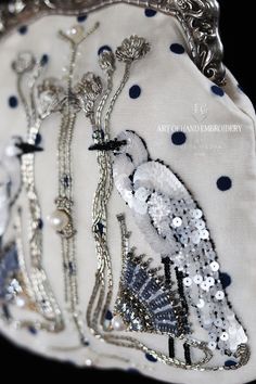 a white purse with blue dots and silver chains on the bottom is decorated with a bird