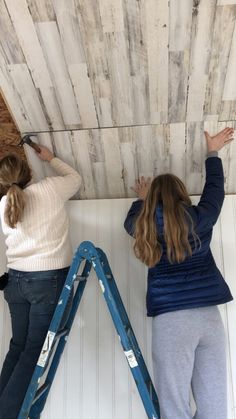 two girls are painting the ceiling with wood planks