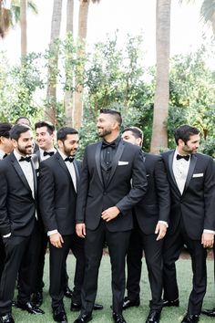 a group of men in tuxedos standing next to each other on the grass