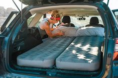 a woman sitting in the back of a blue truck with two mattresses on it