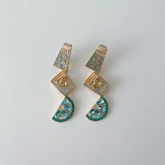 two pairs of earrings with green and blue stones in them on a white table top