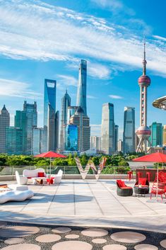 an outdoor patio with red chairs and umbrellas in front of the city skyline