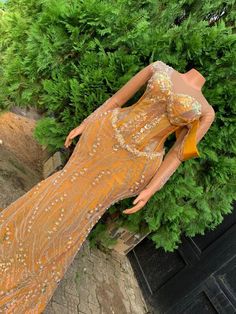 a mannequin dressed in an orange dress standing next to some bushes and trees