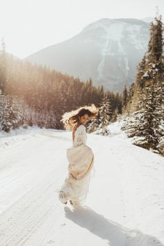 a woman walking down a snow covered road in the middle of winter with her hair blowing in the wind