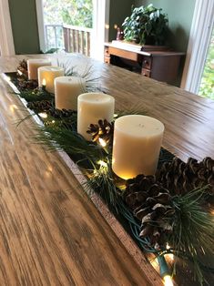 candles are lined up on a long table with pine cones and evergreen branches in the center