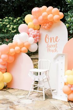 a white chair sitting next to a pink and yellow arch with balloons on the side