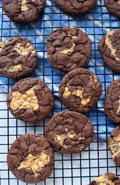 chocolate cookies with peanut butter in the middle on a cooling rack next to a blue and white towel