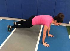 a woman in pink shirt doing push ups on blue and gray floor with wall behind her