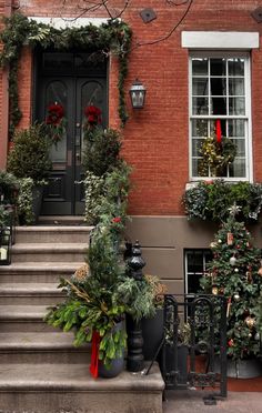 christmas decorations on the front steps of a brick building with holiday wreaths and trees