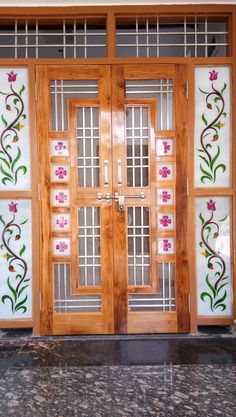 two wooden doors with glass panels and flowers on the side walk in front of a building