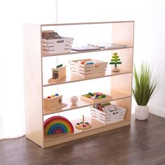 a wooden shelf filled with toys on top of a hard wood floor next to a potted plant