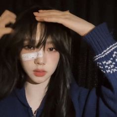 a girl with long black hair wearing a blue sweater and holding her head in front of her face