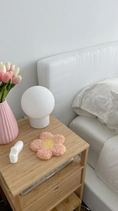 a pink vase with flowers on a small table next to a night stand and bed