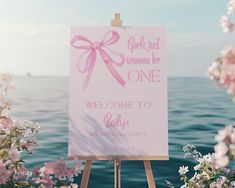 a welcome sign with pink flowers in the foreground and an ocean in the background