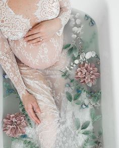 a pregnant woman laying in a bathtub with flowers on the side and her stomach exposed