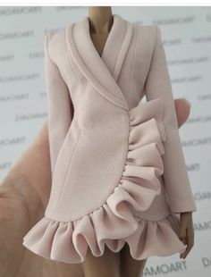 a hand holding a doll wearing a pink dress and jacket with ruffles on it