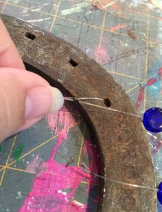 a person is making something out of some kind of metal and blue glass beads on a piece of wood