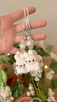 a hand is holding two small sheep keychains in front of a potted plant