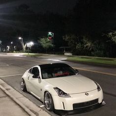 a white sports car parked on the side of the road at night with street lights in the background