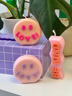 two candles with the words love on them sitting next to a potted plant and box